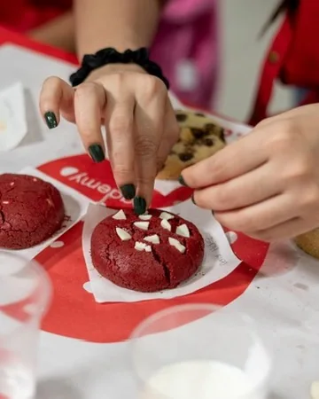 Detalle de manos colocando chocolate sobre una cookie red velvet.